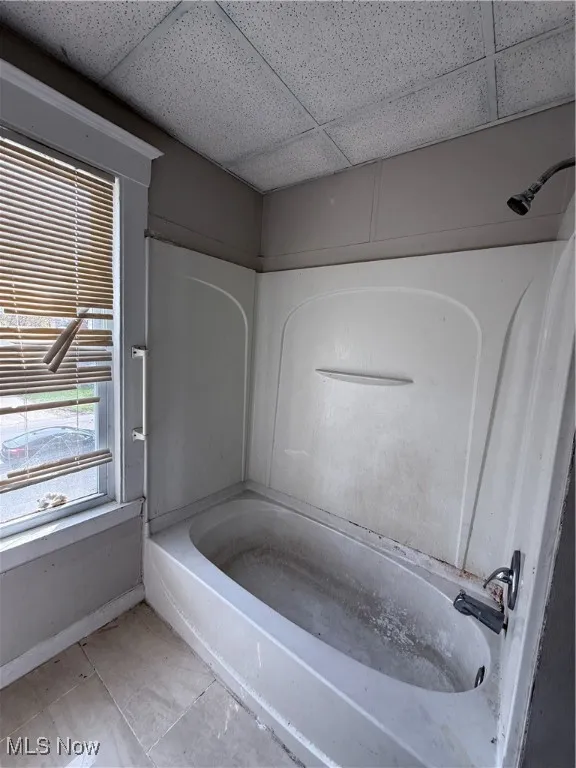 Full bath featuring a drop ceiling, baseboards, and tub / shower combination