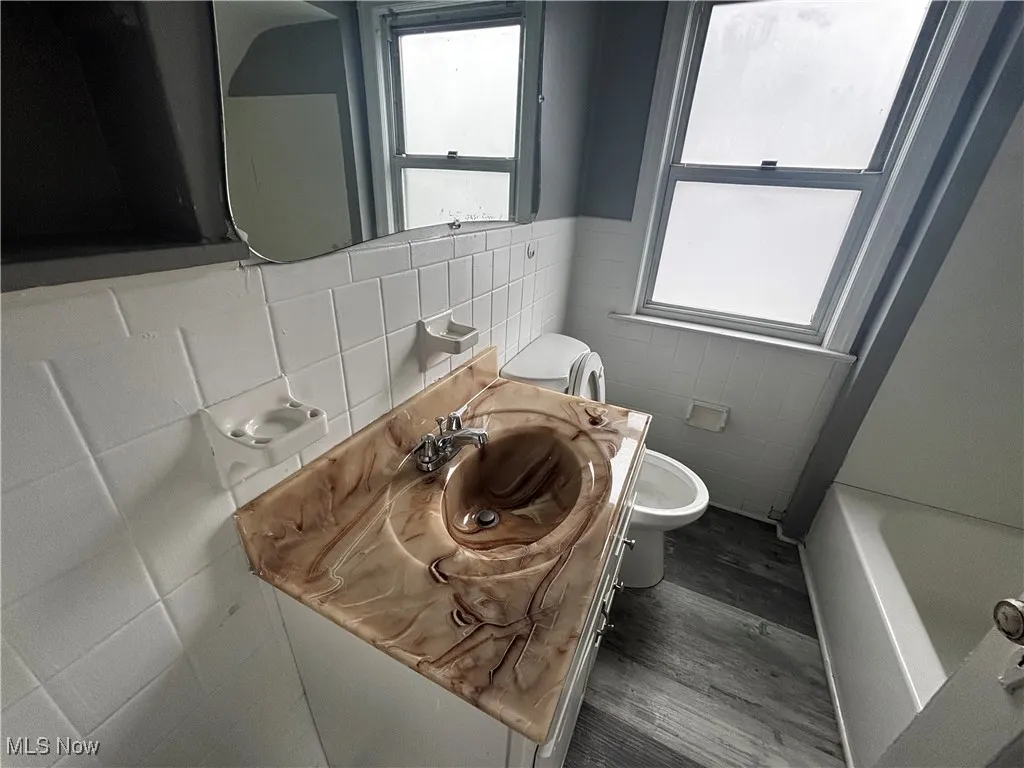 Full bath with tile walls, toilet, wood finished floors, a bathtub, and vanity