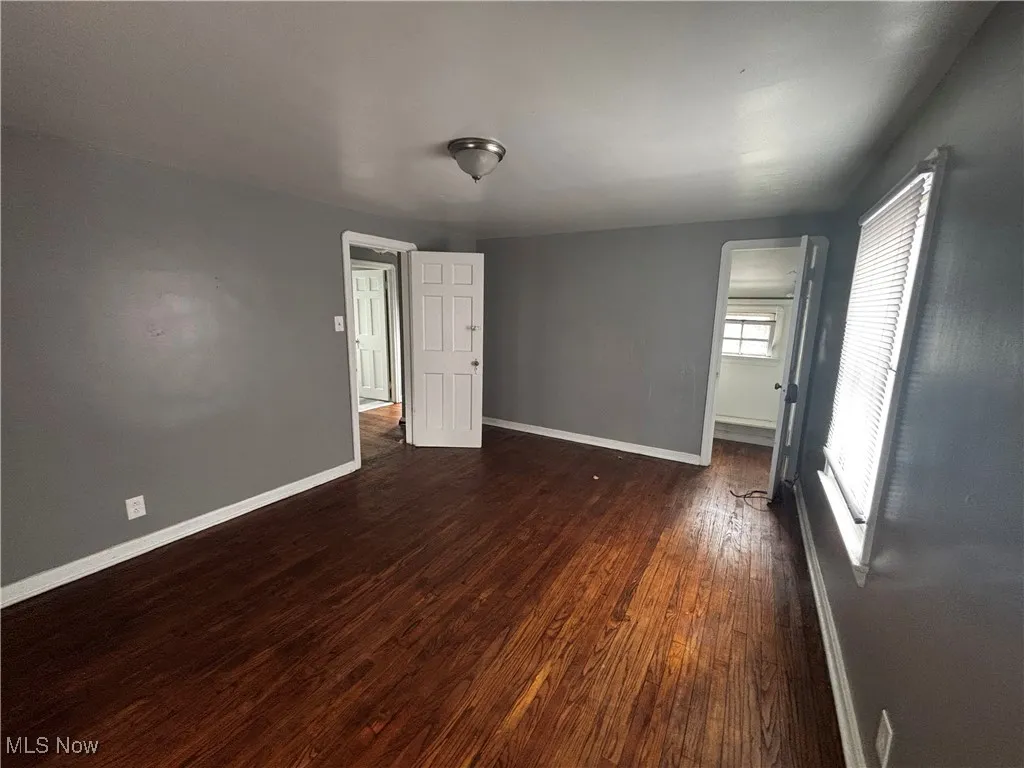 Unfurnished room with baseboards and dark wood-type flooring