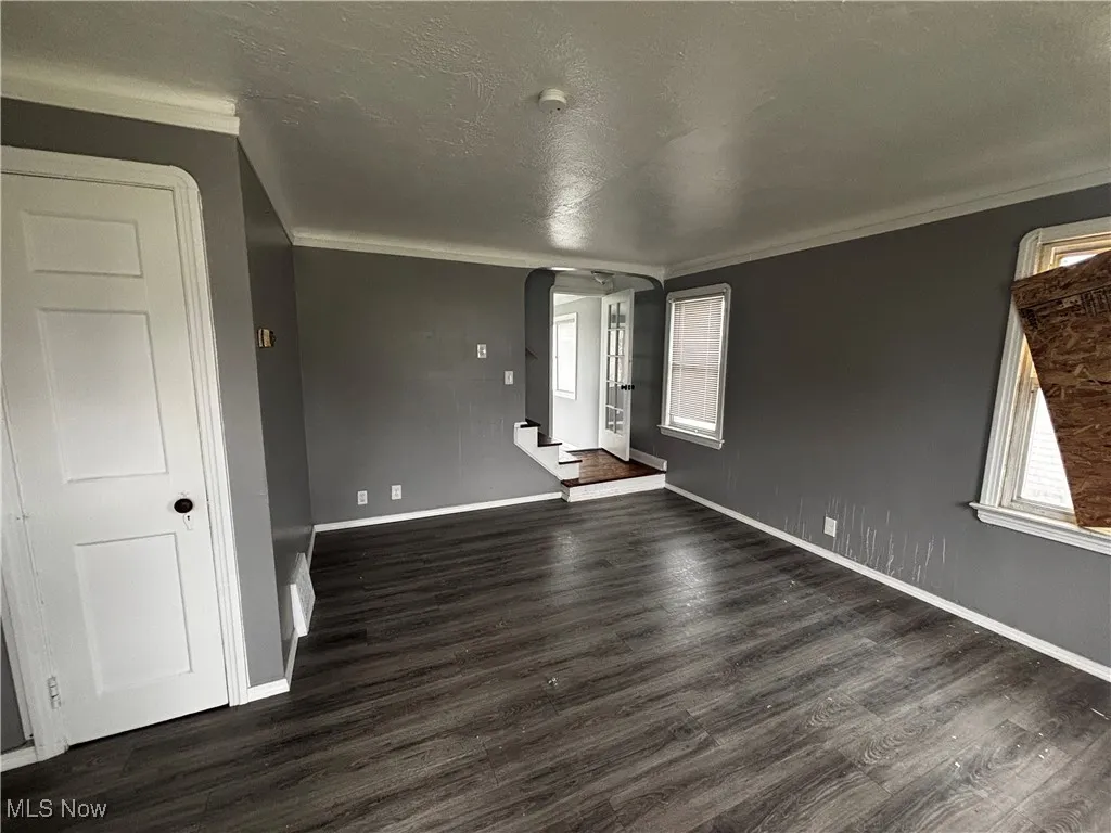 Spare room featuring arched walkways, crown molding, dark wood-type flooring, baseboards, and a textured ceiling