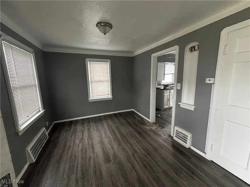 Spare room featuring dark wood-style floors, baseboards, ornamental molding, and a textured ceiling