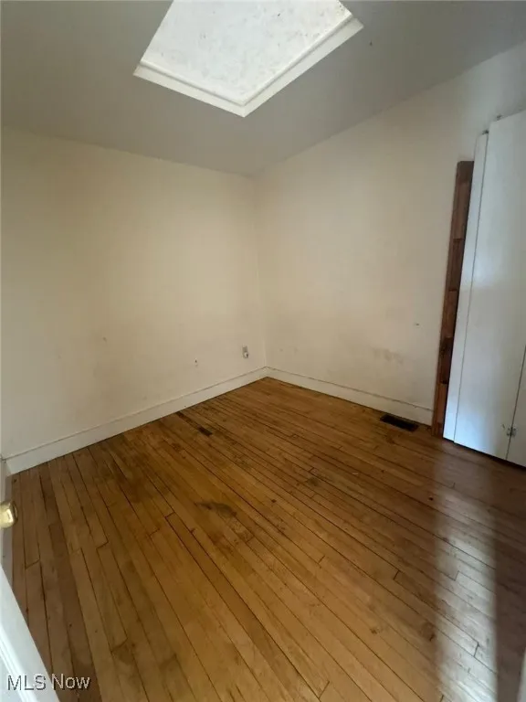 Spare room with a skylight, hardwood / wood-style floors, and baseboards