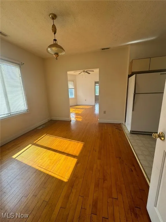 Unfurnished room with hardwood / wood-style floors, baseboards, a textured ceiling, and a ceiling fan