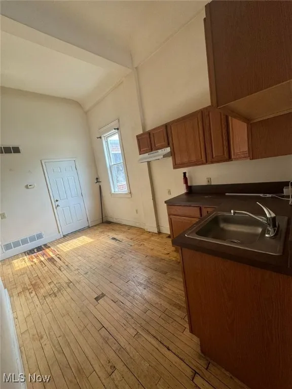 Kitchen with a sink, dark countertops, brown cabinetry, light wood-type flooring, and under cabinet range hood