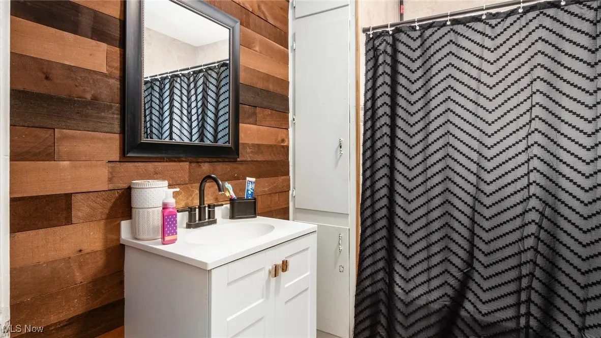 Full bathroom with wood walls, vanity, and a shower with shower curtain
