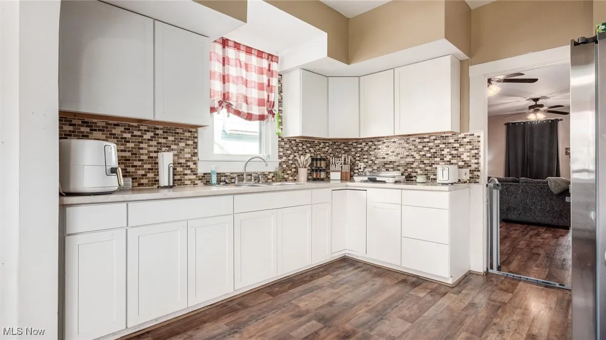 Kitchen featuring a sink, ceiling fan, wood finished floors, light countertops, and decorative backsplash