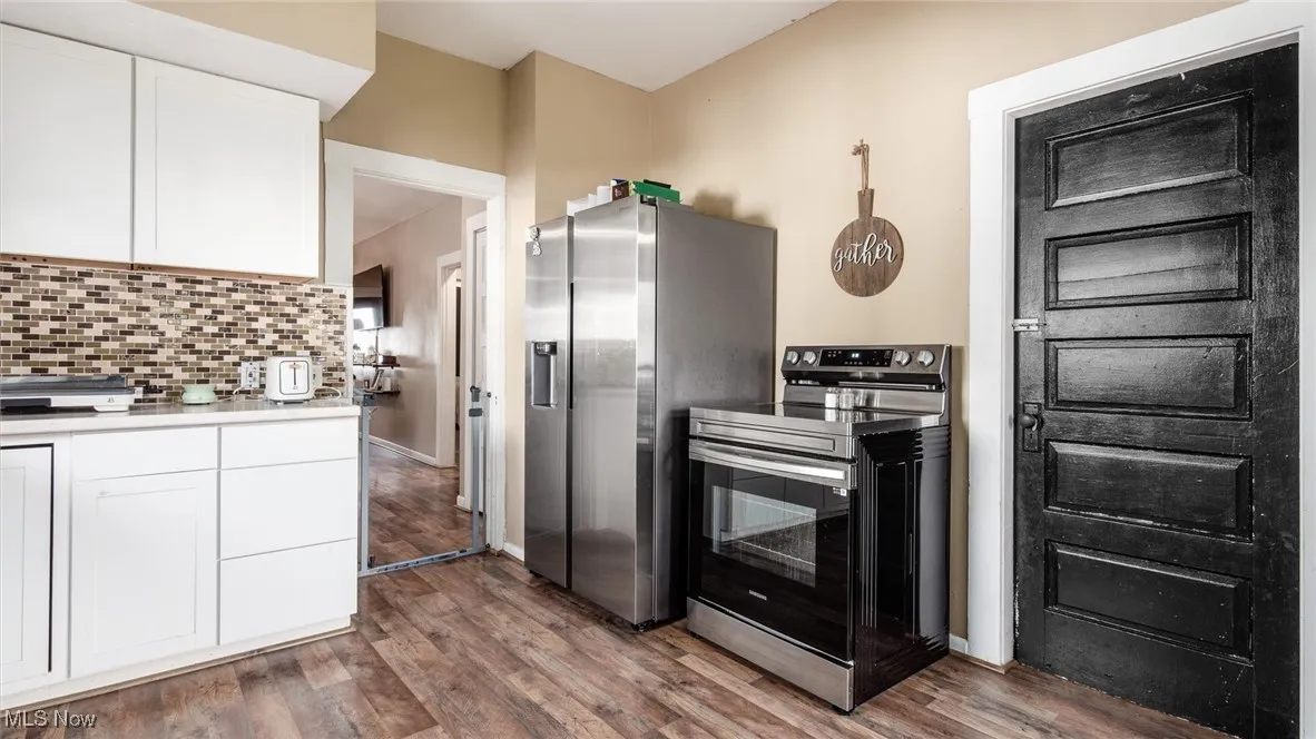 Kitchen featuring stainless steel appliances, white cabinets, wood finished floors, and backsplash