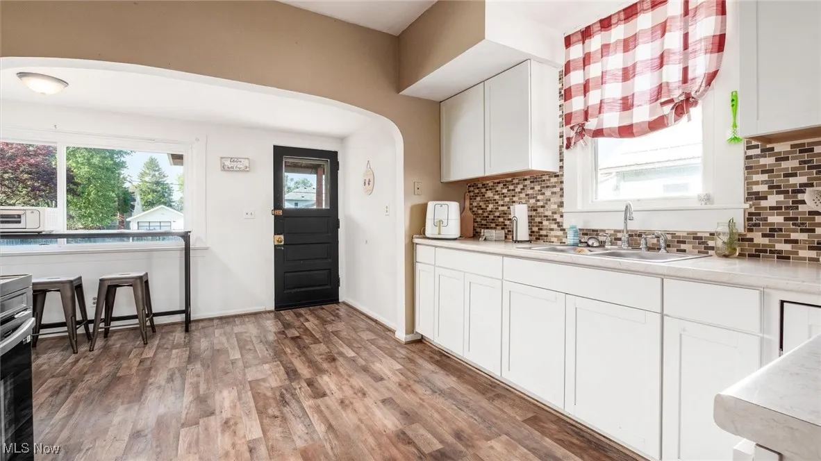 Kitchen featuring a sink, arched walkways, light wood-type flooring, and tasteful backsplash
