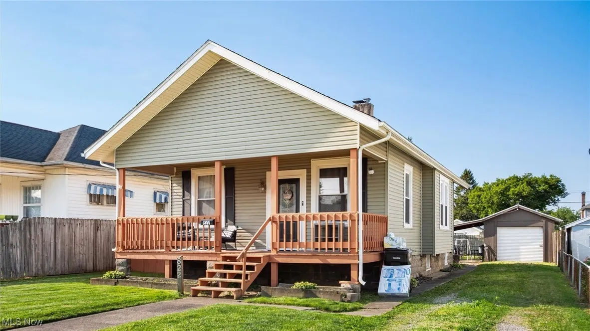 View of front of house with covered porch, a garage, driveway, a chimney, and an outbuilding