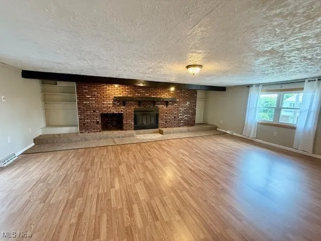 Unfurnished living room featuring a brick fireplace, a textured ceiling, and wood finished floors