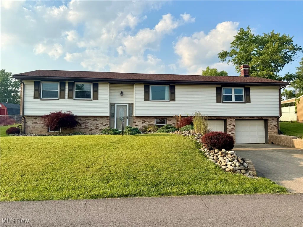Raised ranch with asphalt driveway, an attached garage, brick siding, and a front yard
