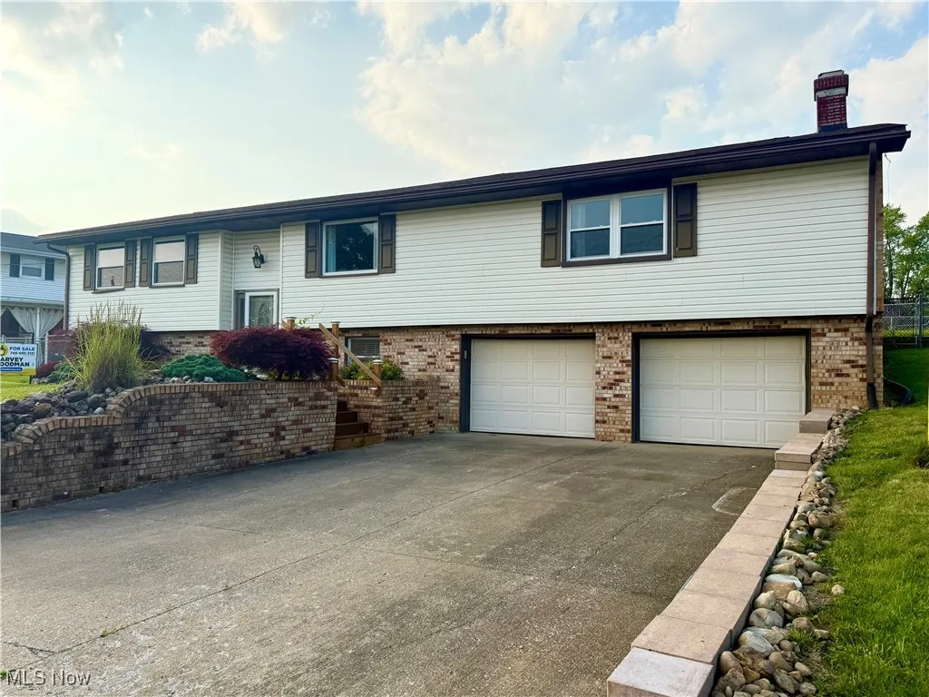 Split foyer home with brick siding, an attached garage, a chimney, and driveway