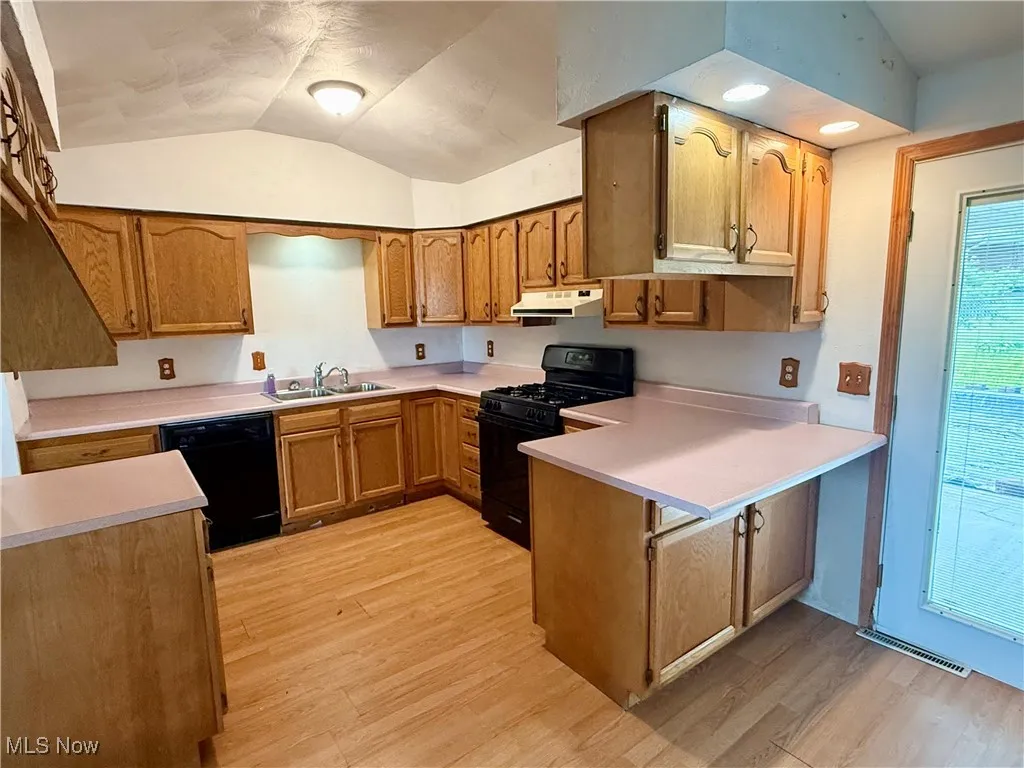 Kitchen with black appliances, a sink, a peninsula, lofted ceiling, and under cabinet range hood