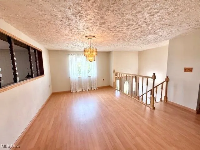 Unfurnished room with a chandelier, wood finished floors, and a textured ceiling