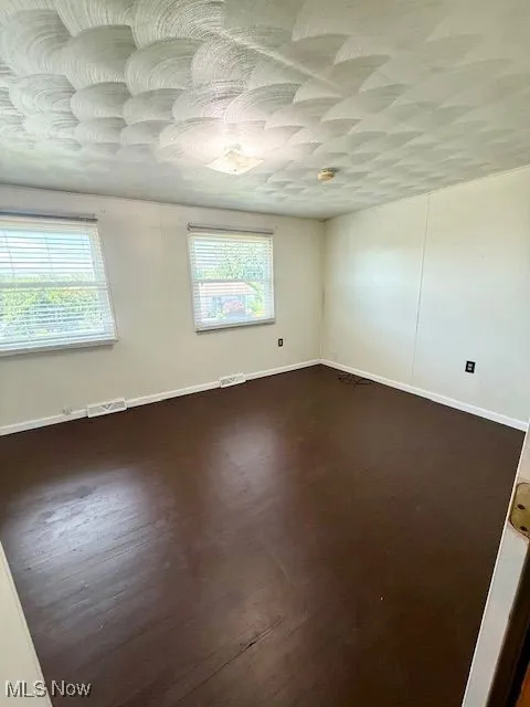 Empty room with healthy amount of natural light and dark wood-style flooring