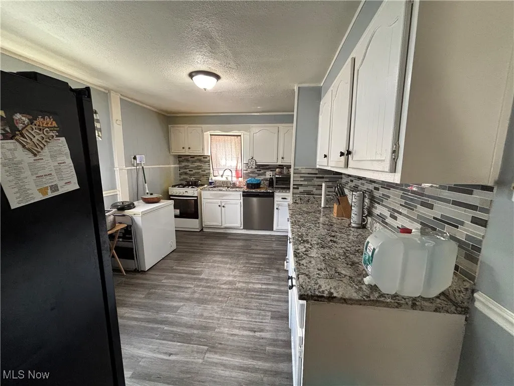 Kitchen featuring freestanding refrigerator, dishwasher, white range with gas stovetop, a sink, and a textured ceiling