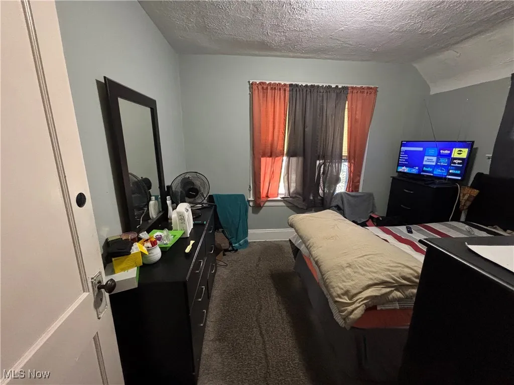 Bedroom with dark colored carpet, a textured ceiling, baseboards, and vaulted ceiling