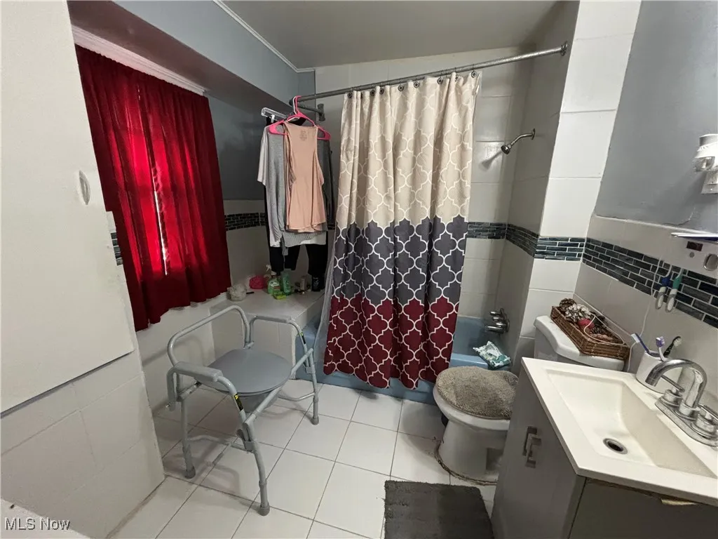 Full bath featuring vanity, toilet, tile walls, shower / tub combo with curtain, and tile patterned floors