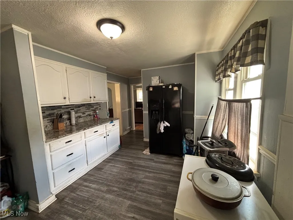 Kitchen featuring black refrigerator with ice dispenser, white cabinetry, backsplash, stone countertops, and dark wood-style floors