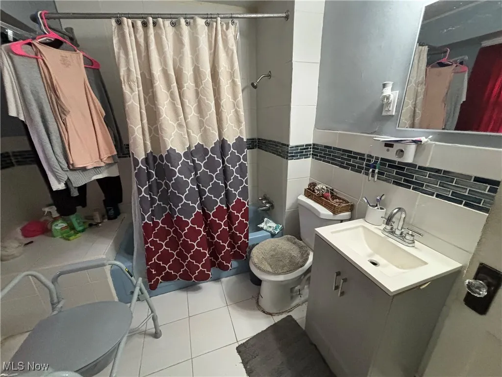 Full bath featuring toilet, shower / bathtub combination with curtain, vanity, tile walls, and tile patterned floors