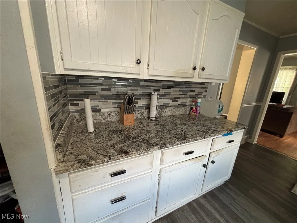 Kitchen featuring dark wood-style floors, tasteful backsplash, white cabinetry, and crown molding