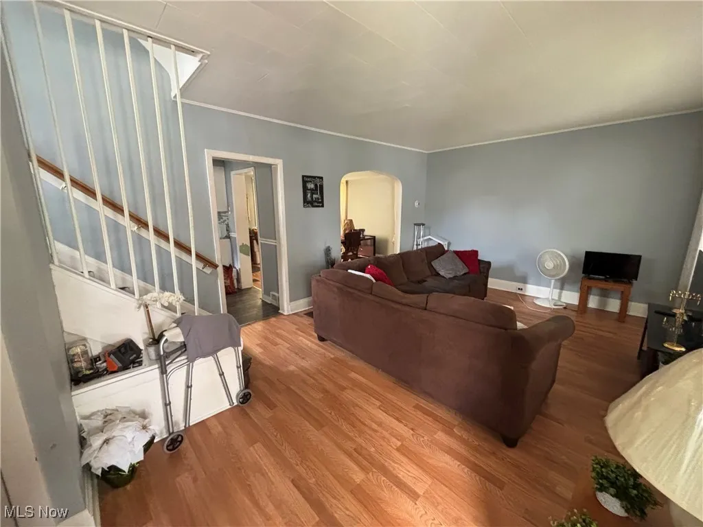 Living area featuring arched walkways, wood finished floors, stairway, baseboards, and crown molding