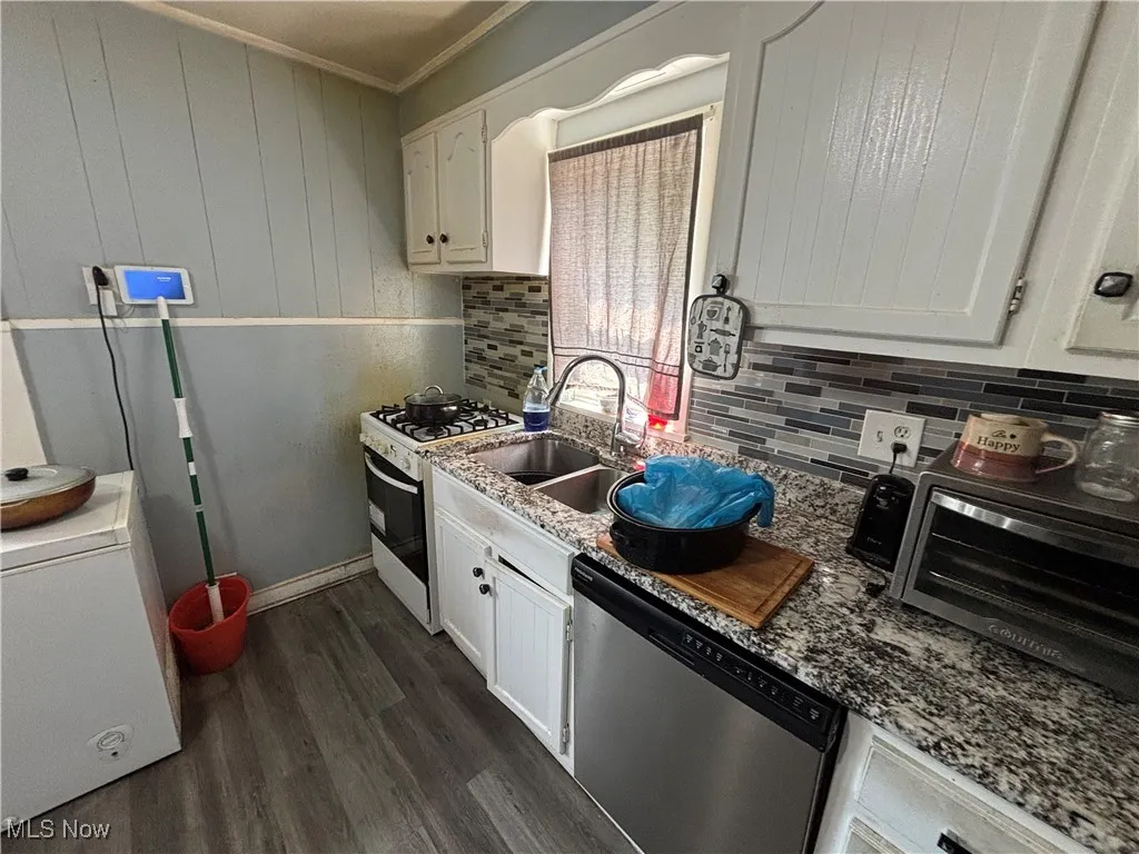 Kitchen with dishwasher, white gas stove, a sink, dark wood finished floors, and white cabinets