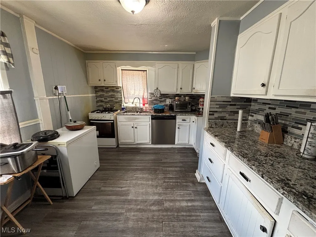 Kitchen with white gas range, dishwasher, a sink, backsplash, and a textured ceiling