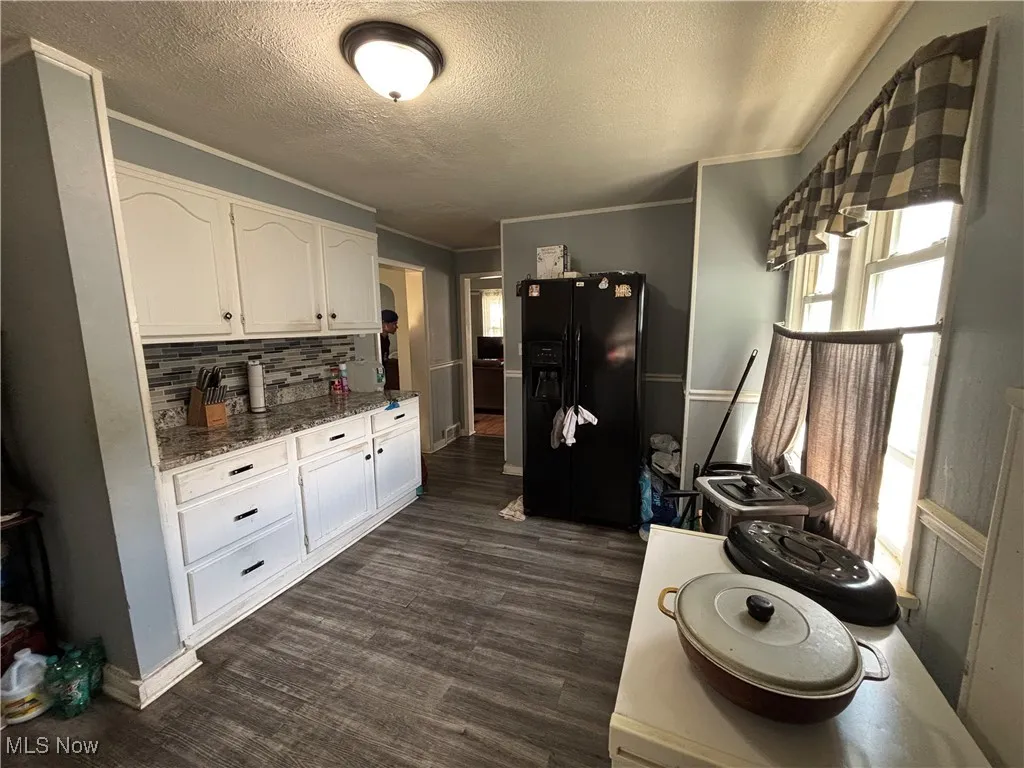 Kitchen featuring black fridge with ice dispenser, plenty of natural light, white cabinets, a textured ceiling, and dark wood finished floors