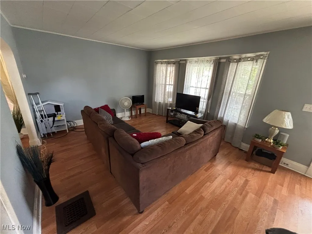 Living area with light wood-type flooring, crown molding, baseboards, and arched walkways