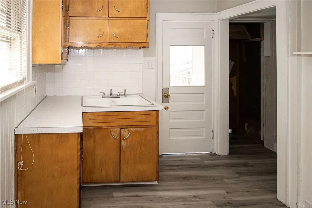 Kitchen featuring a sink, light countertops, brown cabinets, backsplash, and dark wood-style flooring