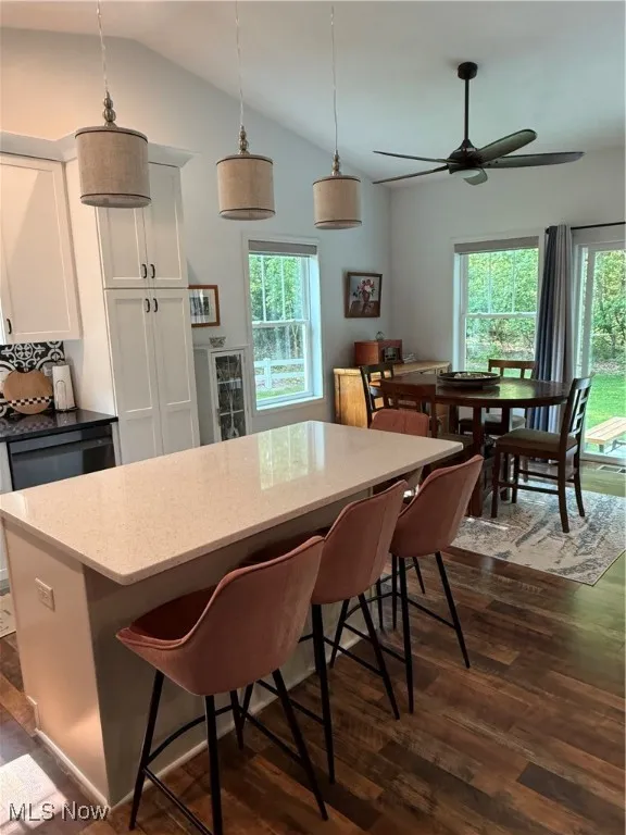 Kitchen with dark wood finished floors, vaulted ceiling, plenty of natural light, an island that seats 4, and white cabinets