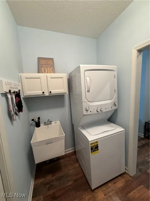 Washroom with stacked washer / drying machine, cabinet space, dark wood-style floors, baseboards, and a textured ceiling
