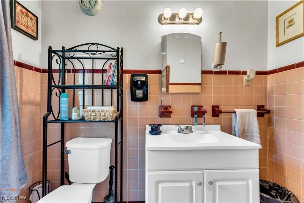 Bathroom with tile walls, vanity, toilet, and a wainscoted wall