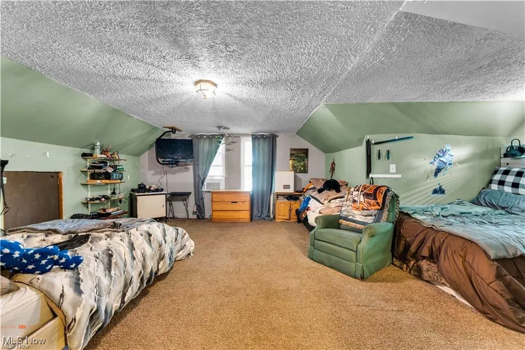 Bedroom with light carpet, lofted ceiling, and a textured ceiling