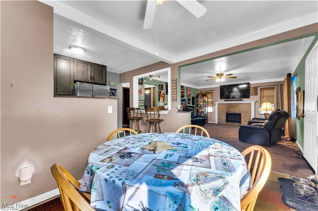 Dining area featuring a ceiling fan, dark carpet, a fireplace, and baseboards