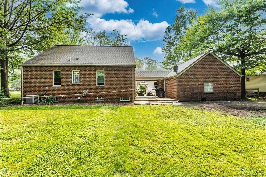 Back of house with a lawn, brick siding, central AC, and a patio area