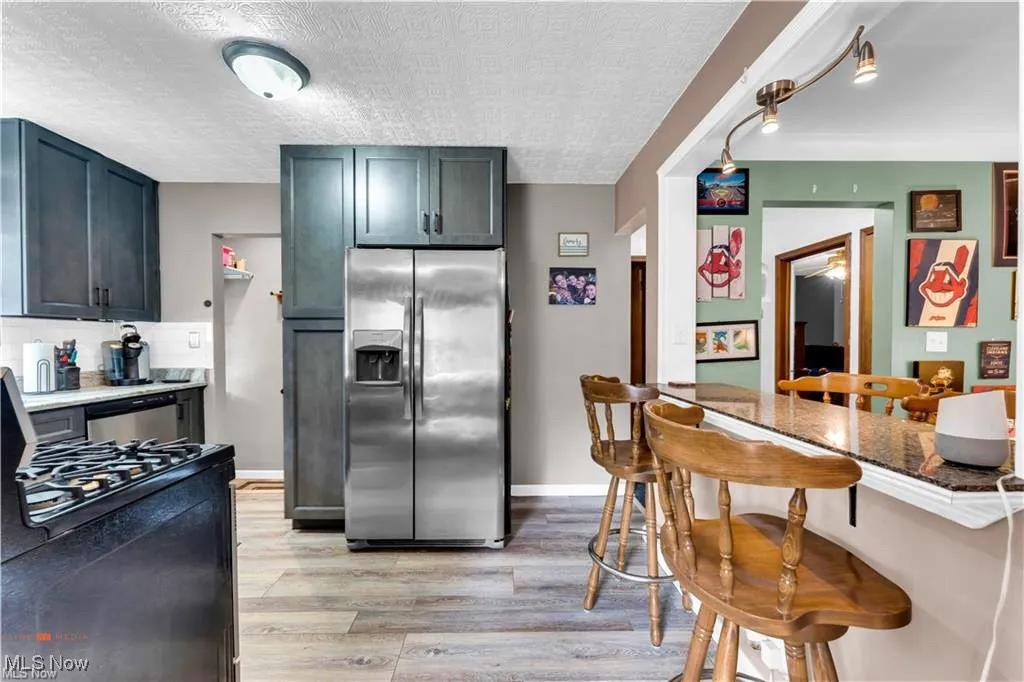 Kitchen featuring appliances with stainless steel finishes, light wood-style floors, a textured ceiling, a kitchen breakfast bar, and backsplash