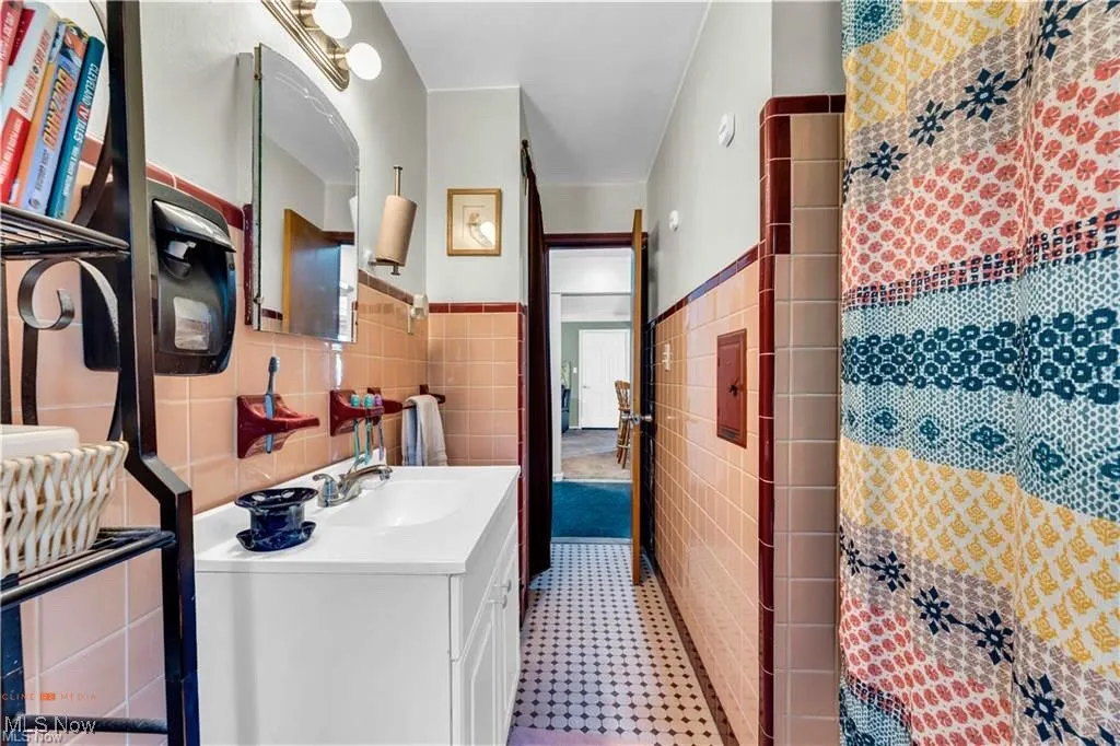 Full bathroom with tile walls, vanity, curtained shower, a wainscoted wall, and tile patterned floors