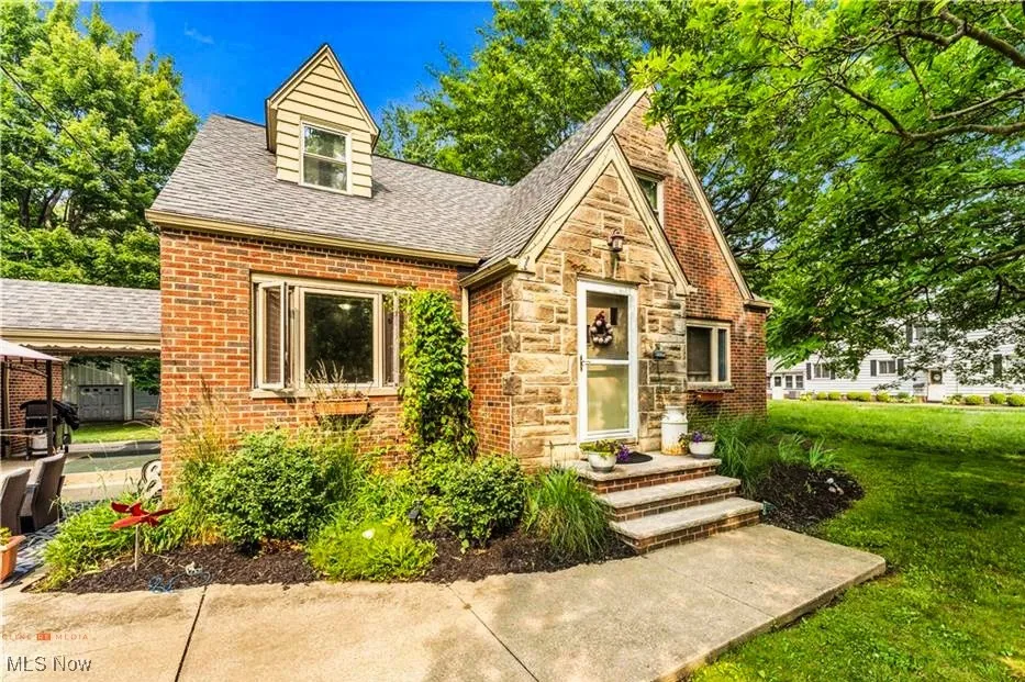 Tudor-style house featuring a front yard, roof with shingles, brick siding, and stone siding