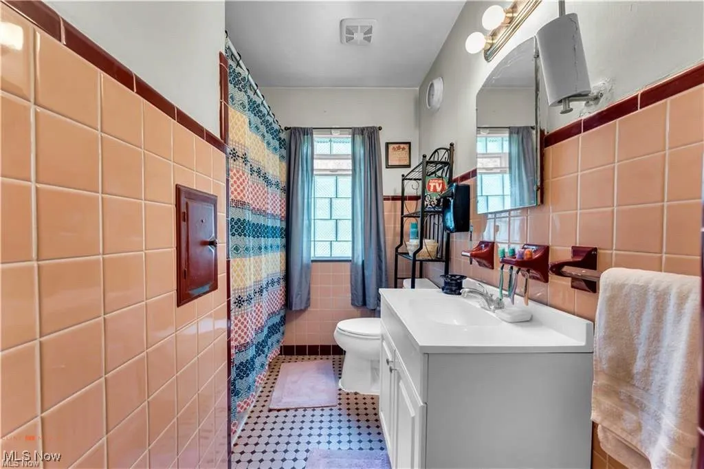 Bathroom with tile walls, toilet, vanity, a wainscoted wall, and a shower with curtain