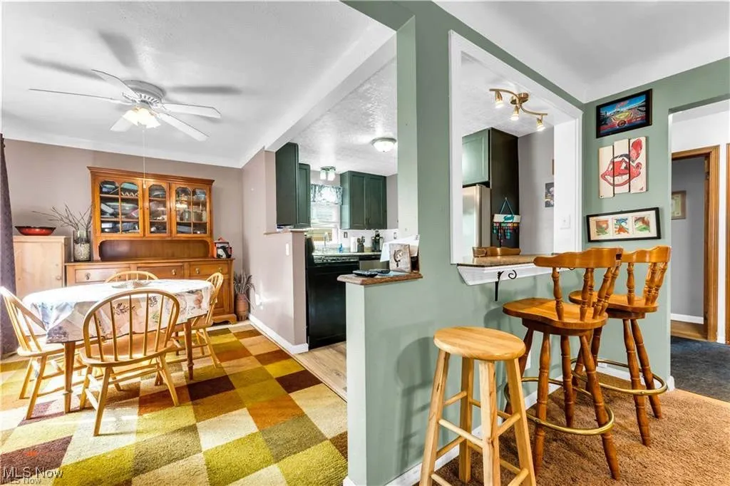 Kitchen with green cabinets, dishwasher, a breakfast bar area, a ceiling fan, and light floors
