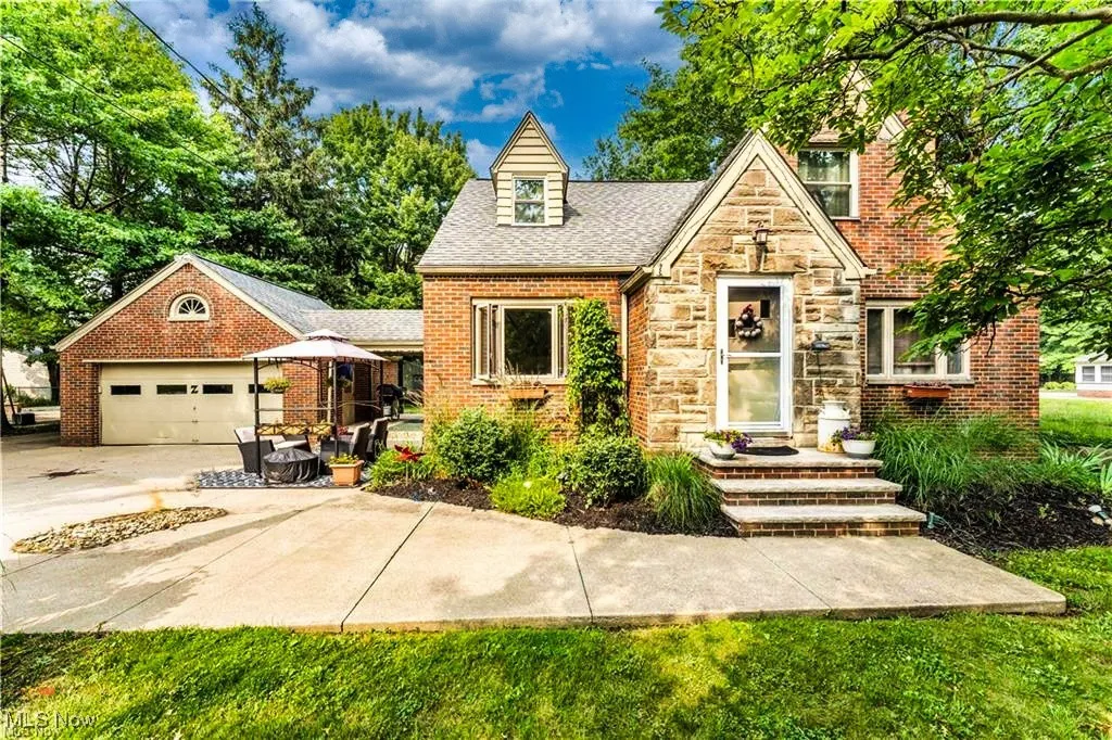 Tudor home with stone siding, an attached garage, concrete driveway, brick siding, and roof with shingles