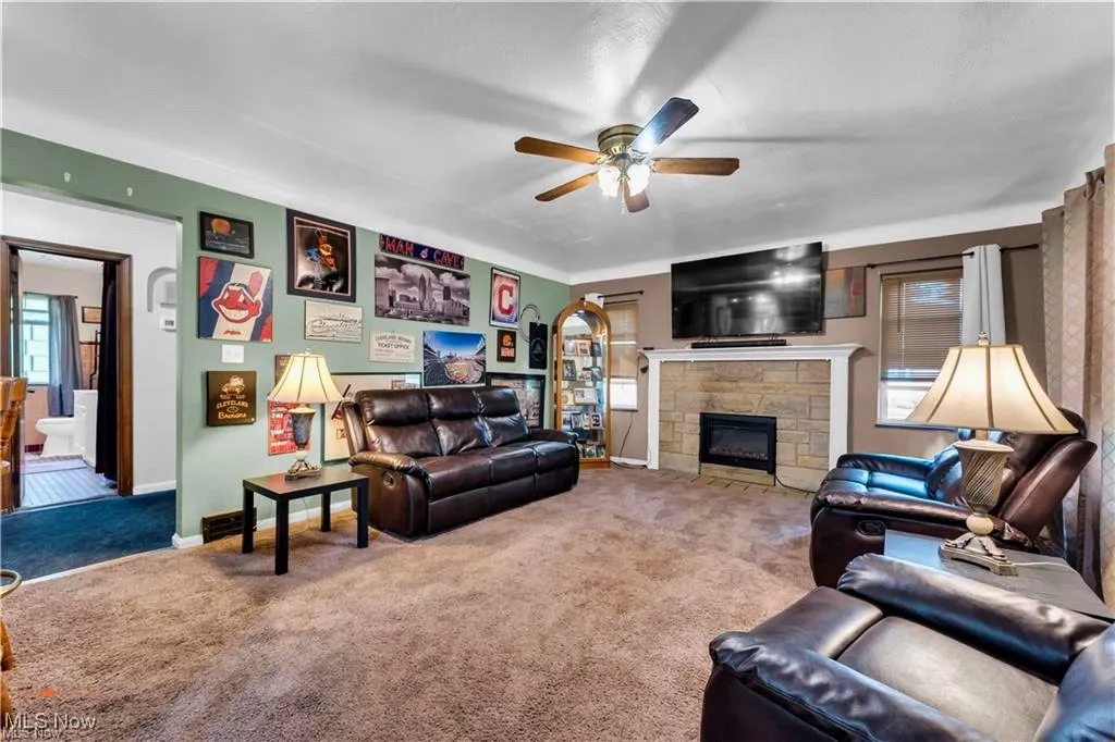 Carpeted living area featuring a ceiling fan, a fireplace, and baseboards