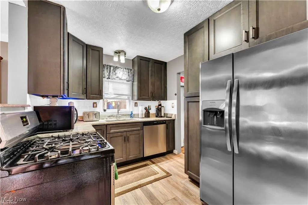 Kitchen featuring stainless steel appliances, a sink, light wood-style floors, light countertops, and a textured ceiling