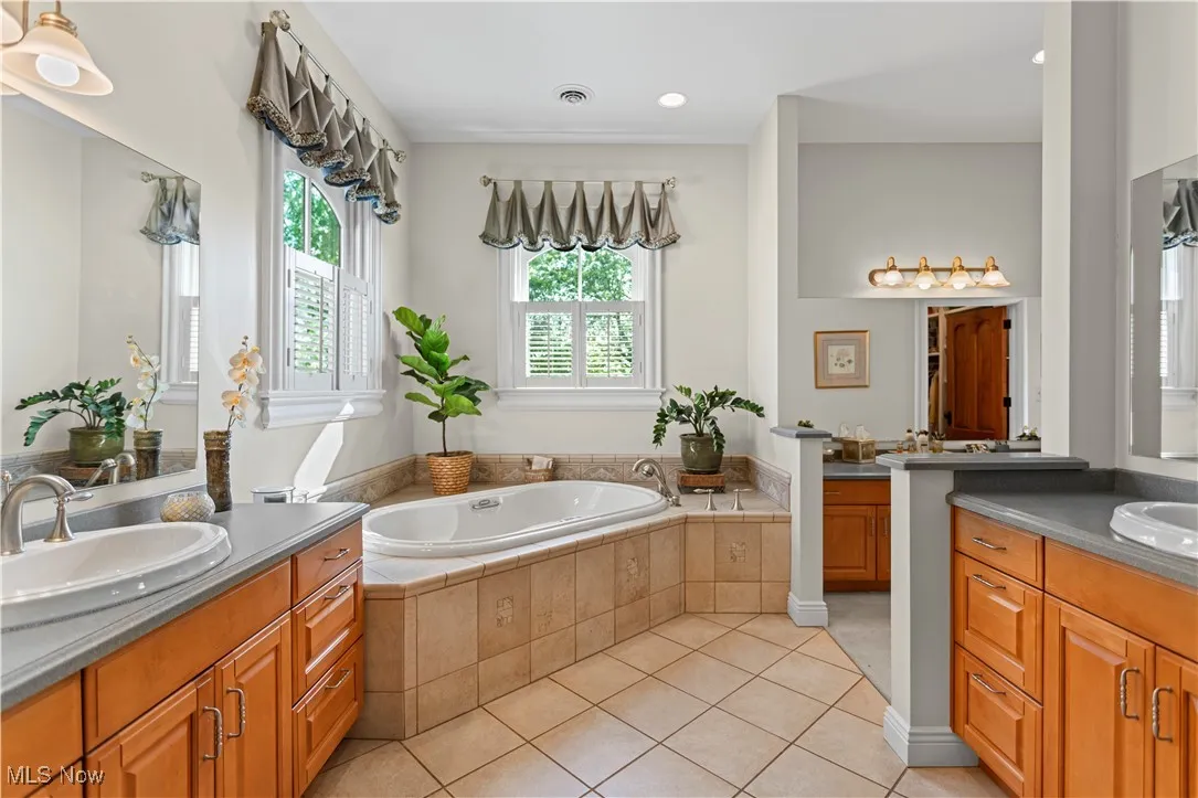 Full bath with two vanities, tile patterned flooring, and a garden tub