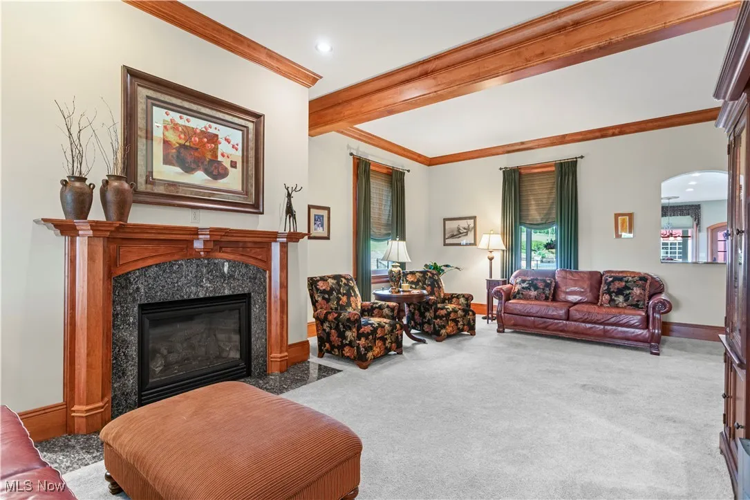 Carpeted living room with ornamental molding, beam ceiling, a premium fireplace, baseboards, and arched walkways