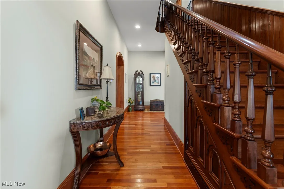 Corridor with wood finished floors, recessed lighting, stairs, baseboards, and arched walkways