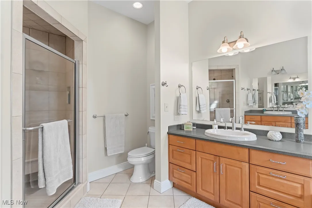 Full bathroom with vanity, tile patterned floors, toilet, a stall shower, and baseboards