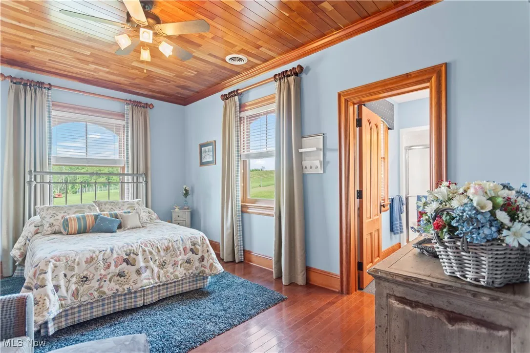 Bedroom with ornamental molding, multiple windows, wood-type flooring, baseboards, and a ceiling fan